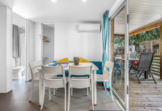 Interior luminoso de cabaña con mesa de comedor, cuatro sillas y vista a terraza cubierta con sillas afuera.