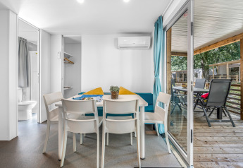 Interno di cabina luminoso con tavolo da pranzo, quattro sedie e vista sul patio coperto e area esterna.