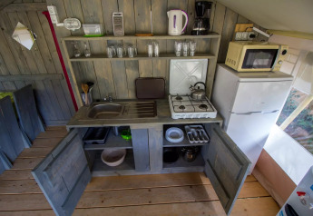 Zona cucina in una tenda safari con fornello a gas, lavandino, frigo, microonde e mobili aperti.