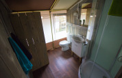 Badkamer in een safaritent met houten vloer, douchecabine, toilet, wastafel en handdoeken aan de muur.