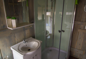 Bagno in una tenda safari con doccia curva in vetro, piccolo lavandino e pareti rivestite in legno.