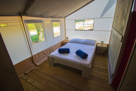 Heller Schlafbereich in einem Safarizelt mit Holzboden, Doppelbett und großen Fenstern.