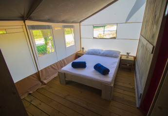 Dormitorio luminoso y acogedor en una tienda safari con piso de madera, cama doble y grandes ventanas.