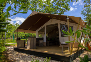 Afbeelding van een safaritent met houten terras en rustieke meubels, omgeven door bomen en groen.