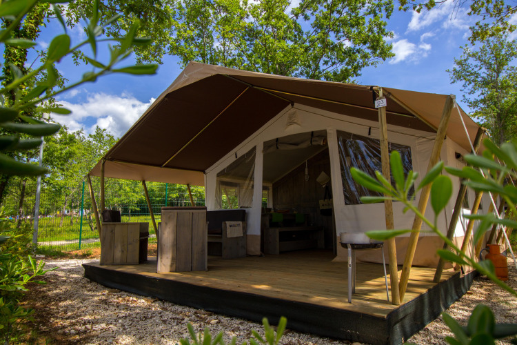 Foto de una tienda safari con terraza de madera y muebles rústicos, rodeada de árboles y vegetación.