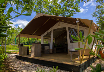 Safari-Zeltunterkunft mit Holzterrasse und rustikalen Möbeln inmitten von grünen Bäumen und Pflanzen.