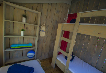 Interno di una tenda safari con letti a castello in legno, scaffali e asciugamani colorati esposti.