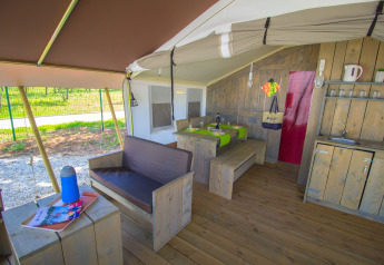 Interno di una tenda safari con mobili in legno, zona pranzo, divano e angolo cottura immersi nella natura.