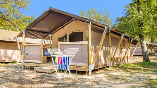 Tente safari Lodge climatisée avec terrasse en bois, étendoir et arbres, située dans un camping ensoleillé.