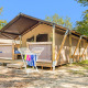 Safari telt Lodge med aircondition, placeret blandt træer, med terrasse og tørrestativ foran under blå himmel.