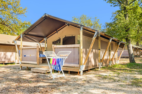 Tienda safari Lodge con aire acondicionado, terraza de madera y tendedero, rodeada de árboles y naturaleza.