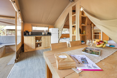 Interno di tenda safari con cucina, tavolo da pranzo, letti e luce naturale in un ambiente accogliente.