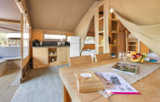 Interieur van een safaritent met keuken, eettafel, bedden en gezellige inrichting vol daglicht.
