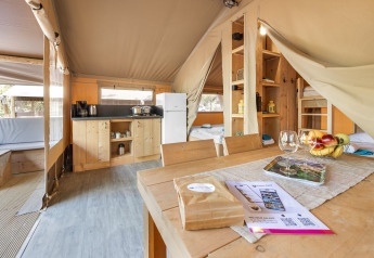 Interno di tenda safari con cucina, tavolo da pranzo, letti e luce naturale in un ambiente accogliente.