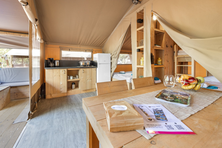 Safari tent interior with kitchen, dining table, beds, and cozy decor, filled with natural light.