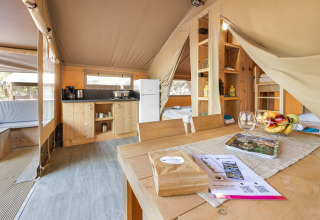 Intérieur d'une tente safari avec cuisine, salle à manger, lits et ambiance chaleureuse.