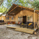 En Safari Tent Lodge med træterrasse, komfortable stole og sofaer, omgivet af træer og natur.