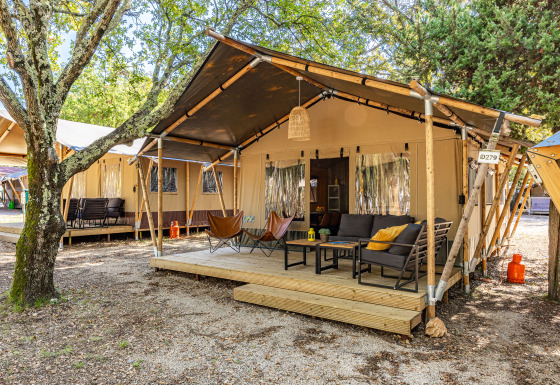 Safari Tent Lodge avec terrasse en bois, fauteuils confortables et canapé, entourée d’arbres et de nature.