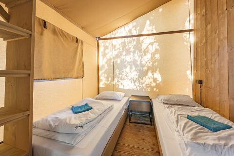 Interior de una tienda safari con dos camas individuales, ropa de cama blanca y luz natural filtrada.
