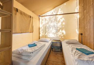 Interior of a safari tent with two single beds, white bedding, wood floor, and natural light filtering in.
