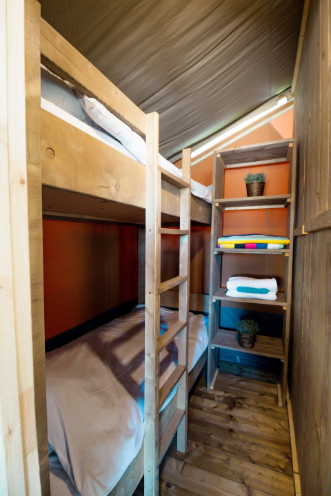 Interno di tenda safari al Camping Polari in Croazia con letti a castello, scaffali e pavimento in legno.