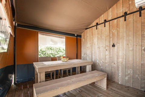 Indvendigt af en safaritelte med træborde, bænke og brune vægge på Camping Polari i Kroatien.