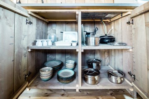 Armario de cocina en tienda safari de Camping Polari en Croacia con platos, ollas y utensilios de cocina.
