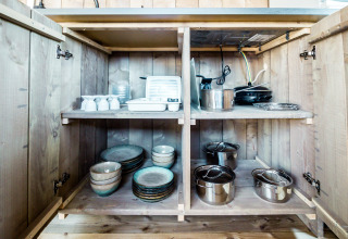 Armario de cocina en tienda safari de Camping Polari en Croacia con platos, ollas y utensilios de cocina.