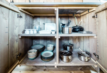 Kitchen cabinet in safari tent at Camping Polari in Croatia, showing dishes, pots, and kitchen appliances.