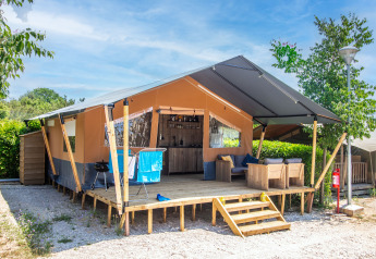 Safari tent with private bathroom and air conditioning, wooden deck, outdoor seating, and shaded roof.