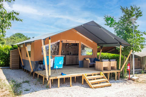 Tente safari avec salle de bain privée et climatisation, terrasse en bois et meubles de jardin.