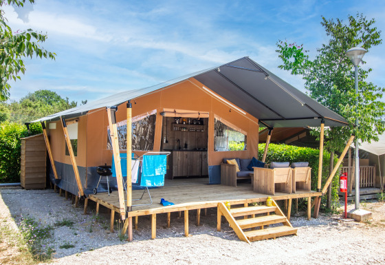 Safari tent met eigen sanitair en airconditioning, houten veranda, zithoek en buitenmeubilair.
