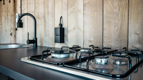 Cocina moderna con estufa de gas y grifo negro en tienda safari de Camping Polari, Croacia, con pared de madera.