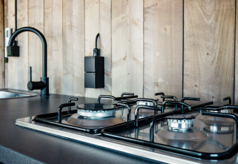 Modern kitchen in a safari tent at Camping Polari, Croatia with gas stove, black faucet and wood walls.