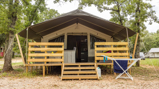 Luxe safaritent met overdekte veranda en houten hekwerk, omgeven door bomen en natuur.