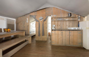 Interno di una tenda safari di lusso con arredi in legno, tavolo da pranzo, angolo cottura e camera.