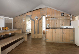Interno di una tenda safari di lusso con arredi in legno, tavolo da pranzo, angolo cottura e camera.