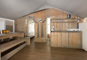 Interno di una tenda safari di lusso con arredi in legno, tavolo da pranzo, angolo cottura e camera.