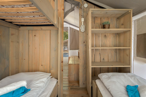 Vista interior de la Safari Tent Luxury con dos camas individuales, estantería de madera y decoración acogedora.