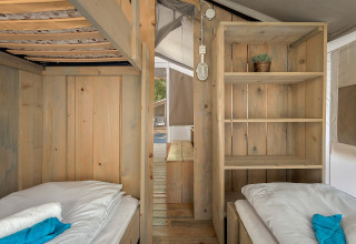 Vista interior de la Safari Tent Luxury con dos camas individuales, estantería de madera y decoración acogedora.