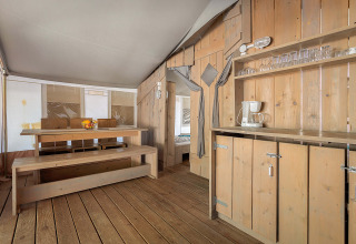 Interior de la Safari Tent Luxury con bancos y mesa de madera, cocina y vajilla para una estancia cómoda.