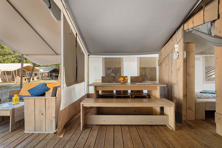 Vista interior de Safari Tent Luxury con muebles de madera, mesa de comedor y sofá bajo una carpa.