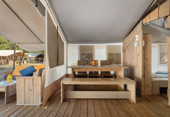 Vista interna della Safari Tent Luxury con mobili in legno, tavolo da pranzo e divano sotto il tendone.