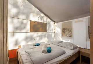 Interior de Safari Tent Luxury con cama cómoda, sábanas blancas y luz natural a través de lonas.