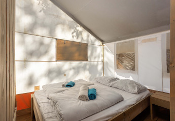 Interior de Safari Tent Luxury con cama cómoda, sábanas blancas y luz natural a través de lonas.