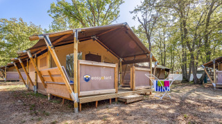 Tienda safari en un camping con terraza de madera y tendal para toallas rodeada de árboles y naturaleza.