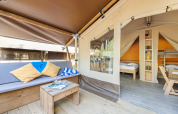 Tenda safari accogliente con divano, cuscini, tavolino in legno e letti visibili nell’area notte.