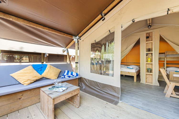 Cozy safari tent with wooden furniture, sofa with pillows, and beds visible in the sleeping area.