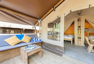 Tienda safari acogedora con sofá, cojines, mesa de madera y camas visibles en el área de dormir.