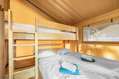 Vista interna di una tenda safari con letto a castello e letto matrimoniale, lenzuola bianche e asciugamani.